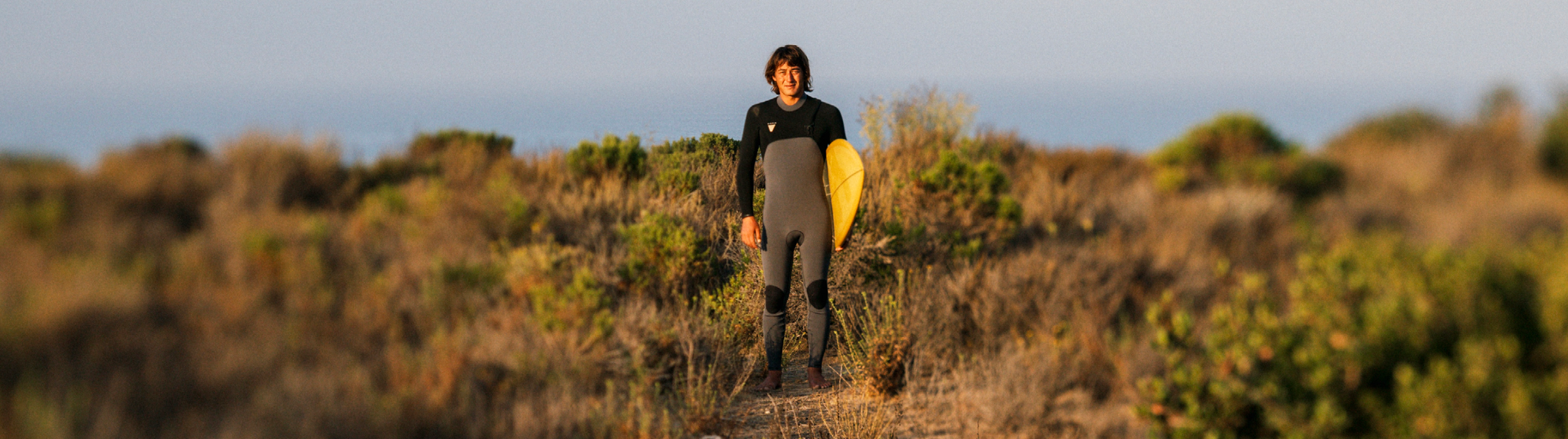 Surfer w piance Vissla Natural Seas z deska na wzgorzu