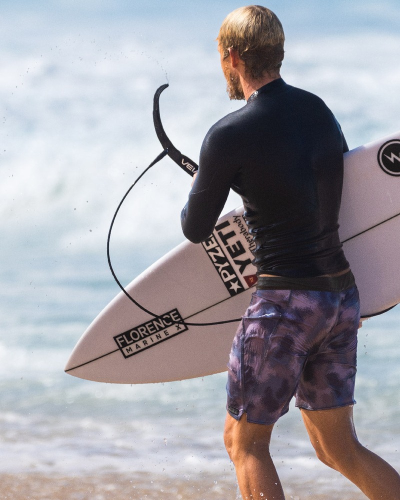 Surfer z leashem VEIA Explorer i deską na plaży